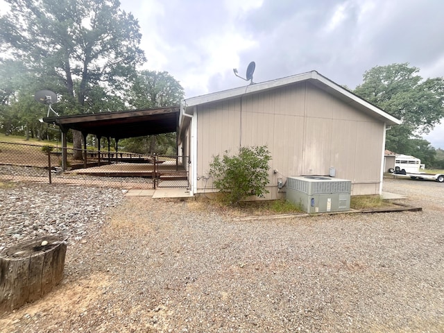 view of side of home featuring gravel driveway, central AC unit, an attached carport, and fence