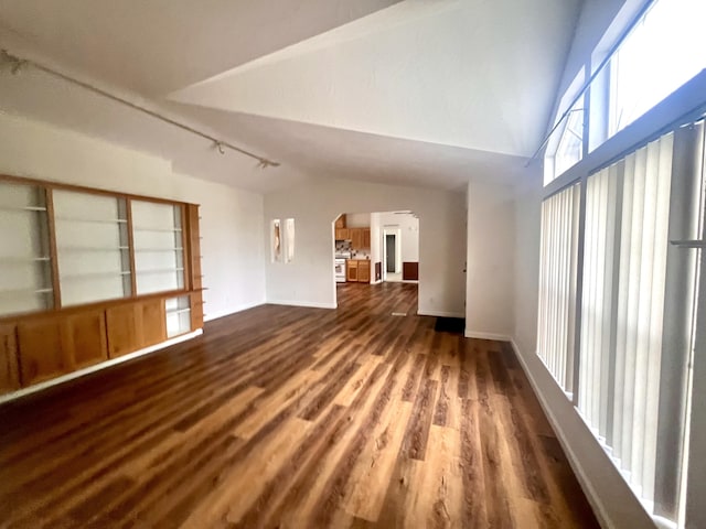 unfurnished living room with track lighting, wood finished floors, arched walkways, baseboards, and lofted ceiling