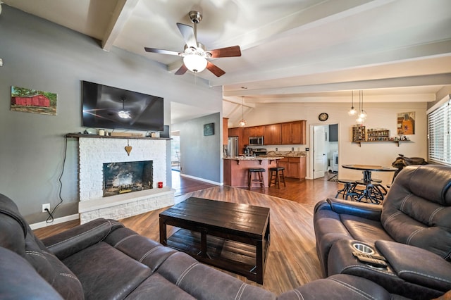 living area with baseboards, ceiling fan, wood finished floors, and beamed ceiling