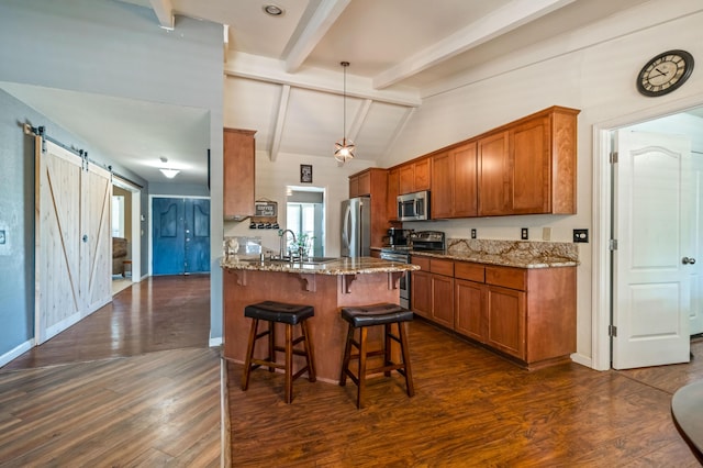 kitchen featuring appliances with stainless steel finishes, light stone countertops, brown cabinets, a barn door, and a breakfast bar