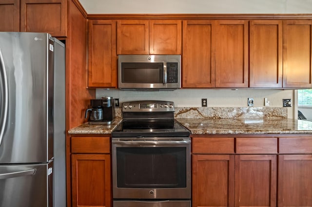 kitchen featuring appliances with stainless steel finishes, brown cabinetry, and light stone countertops
