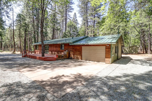 view of side of home with a garage, metal roof, a standing seam roof, a wooden deck, and driveway