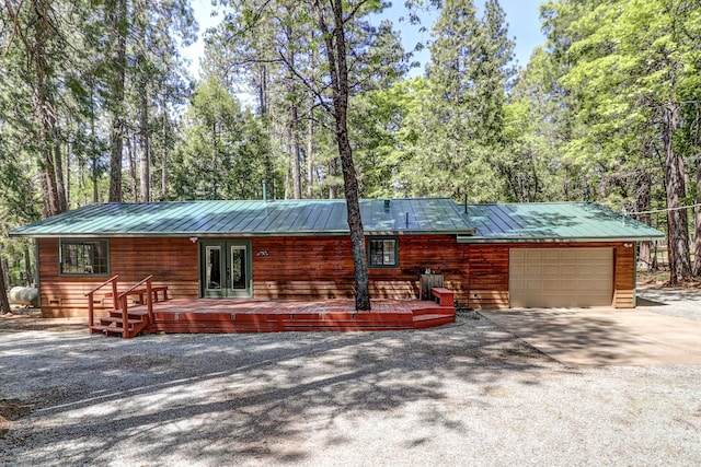 rear view of property featuring an attached garage, metal roof, driveway, and french doors
