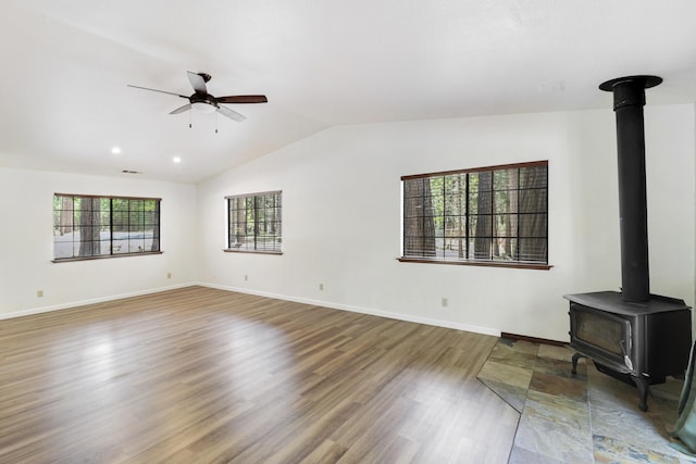unfurnished living room with a wood stove, vaulted ceiling, ceiling fan, wood finished floors, and baseboards