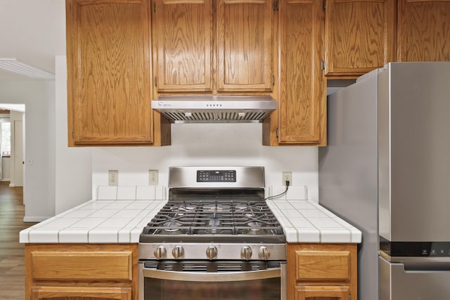 kitchen featuring appliances with stainless steel finishes, under cabinet range hood, tile countertops, and wood finished floors