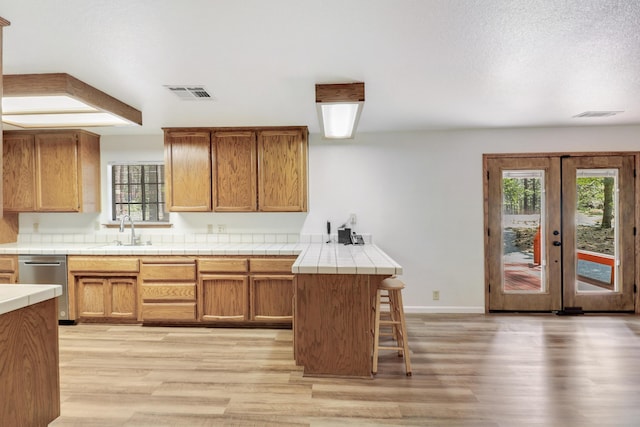 kitchen featuring a sink, tile counters, dishwasher, and light wood finished floors