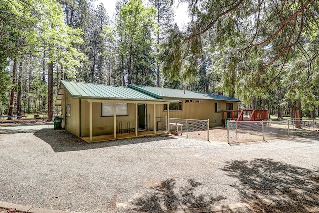 back of house with fence, metal roof, a wooden deck, and view of scattered trees