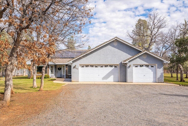 single story home with dirt driveway, a front yard, solar panels, an attached garage, and stucco siding