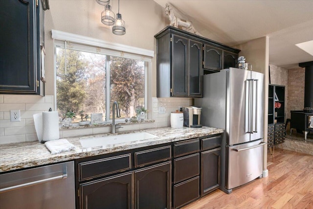 kitchen featuring light wood-style flooring, a wood stove, a sink, stainless steel appliances, and light stone countertops