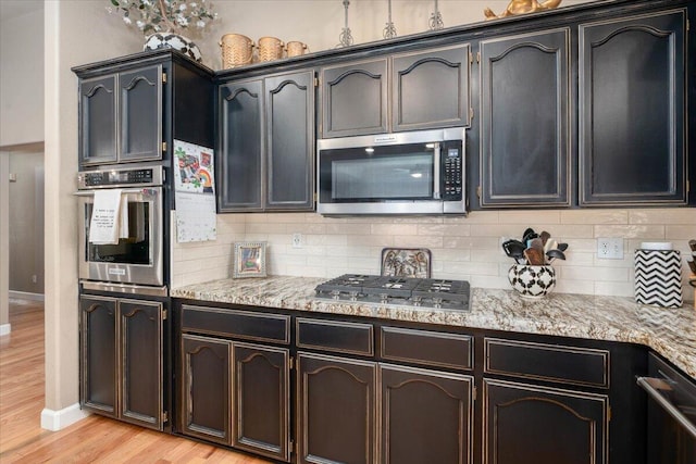 kitchen featuring appliances with stainless steel finishes, light wood-style floors, baseboards, and backsplash