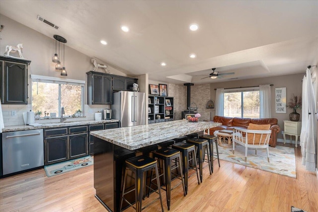 kitchen featuring light wood-style flooring, a wood stove, a sink, appliances with stainless steel finishes, and backsplash