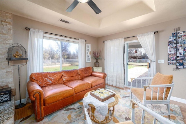 living area featuring visible vents, a ceiling fan, plenty of natural light, and a tray ceiling