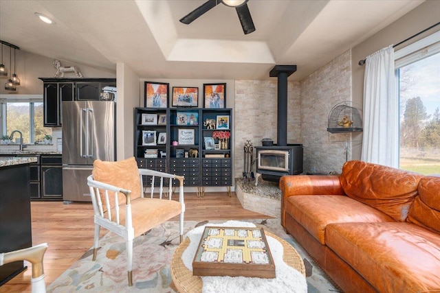 living room with a ceiling fan, a wealth of natural light, a wood stove, and light wood-style flooring