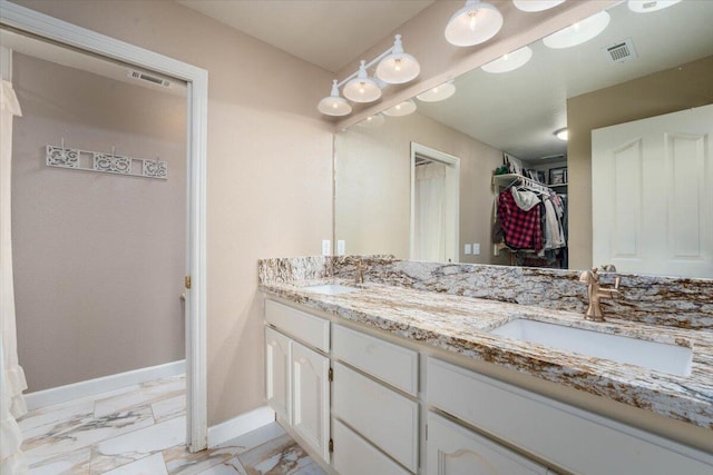 bathroom with a sink, marble finish floor, a walk in closet, double vanity, and baseboards