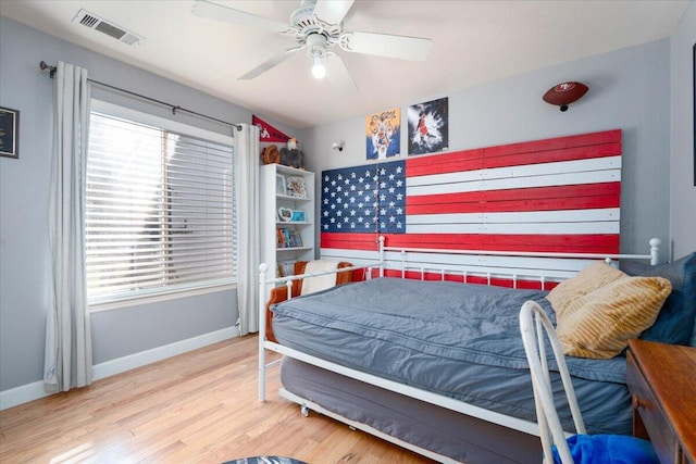 bedroom with baseboards, visible vents, wood finished floors, and multiple windows