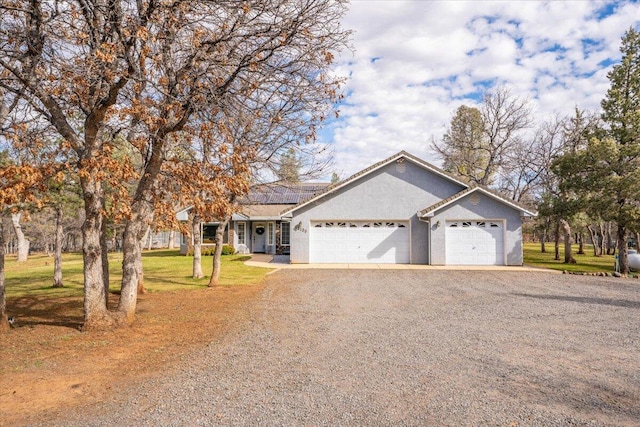 ranch-style home featuring a front yard, gravel driveway, an attached garage, solar panels, and stucco siding