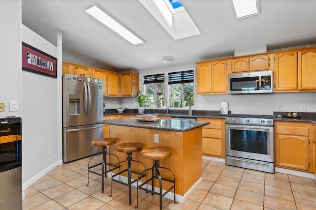 kitchen with a kitchen island, appliances with stainless steel finishes, light tile patterned floors, and lofted ceiling with skylight
