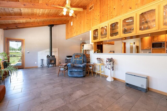 sitting room featuring wood ceiling, ceiling fan, beamed ceiling, and a wood stove