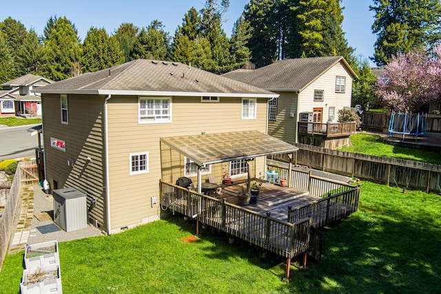 rear view of house featuring a trampoline, a fenced backyard, a shingled roof, a wooden deck, and crawl space