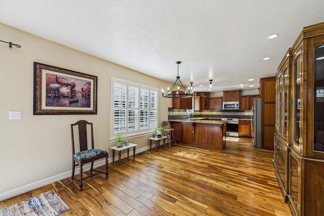 kitchen with stainless steel appliances, baseboards, dark wood-type flooring, a peninsula, and a notable chandelier