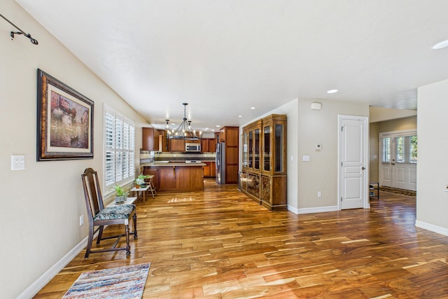 interior space featuring brown cabinetry, stainless steel appliances, an inviting chandelier, and wood finished floors