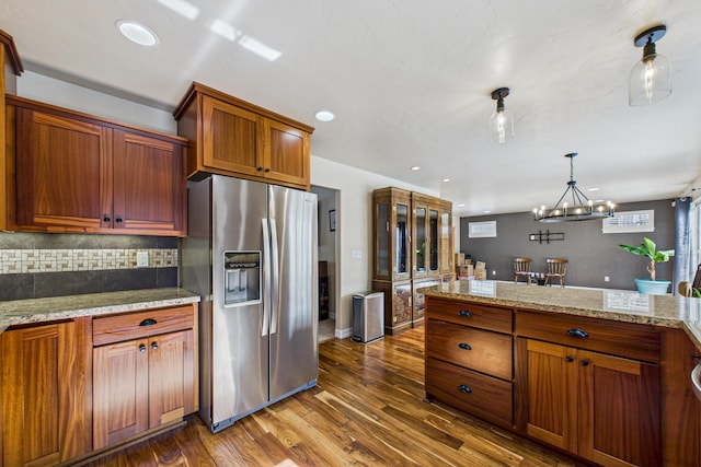 kitchen with decorative backsplash, an inviting chandelier, wood finished floors, brown cabinetry, and stainless steel fridge with ice dispenser