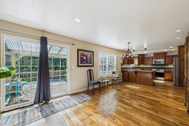 kitchen featuring visible vents, stainless steel appliances, wood-type flooring, an inviting chandelier, and a peninsula