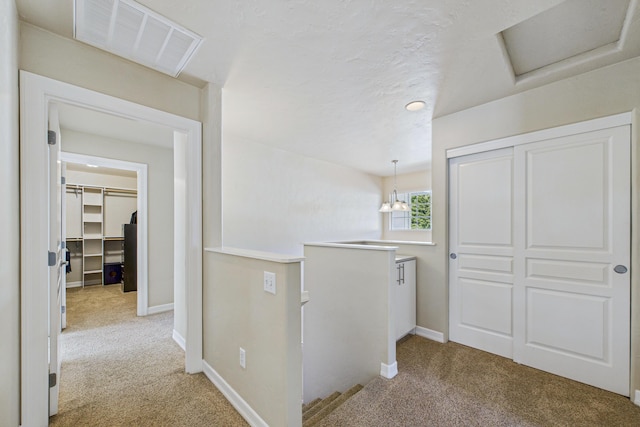 hallway featuring an upstairs landing, visible vents, carpet, and baseboards