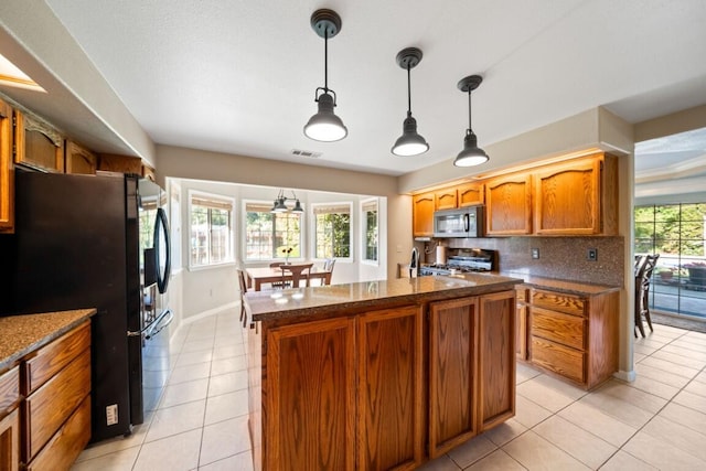 3301 Bridger Dr, Redding, CA 96002 - kitchen with stainless steel microwave, freestanding refrigerator, gas range oven, light tile patterned flooring, and hanging light fixtures