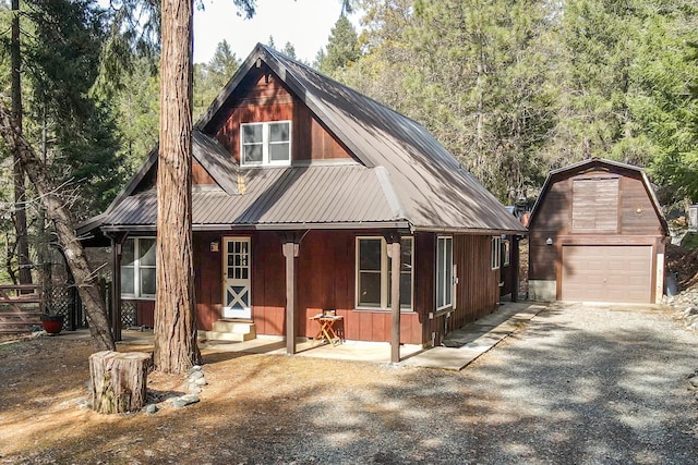 rustic home featuring driveway, metal roof, an outbuilding, a detached garage, and a view of trees