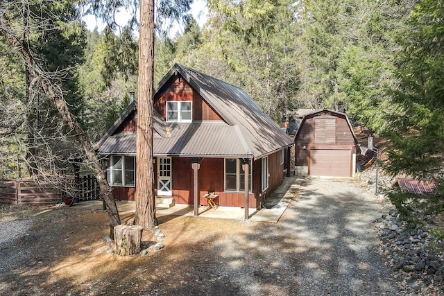 chalet / cabin featuring a porch, a forest view, driveway, metal roof, and an outbuilding