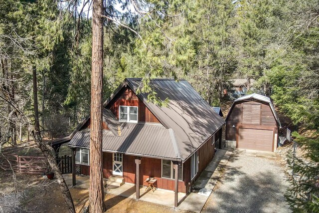 chalet / cabin featuring a forest view, metal roof, a detached garage, an outdoor structure, and gravel driveway