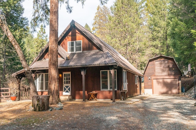 chalet / cabin with covered porch, driveway, metal roof, a garage, and an outdoor structure