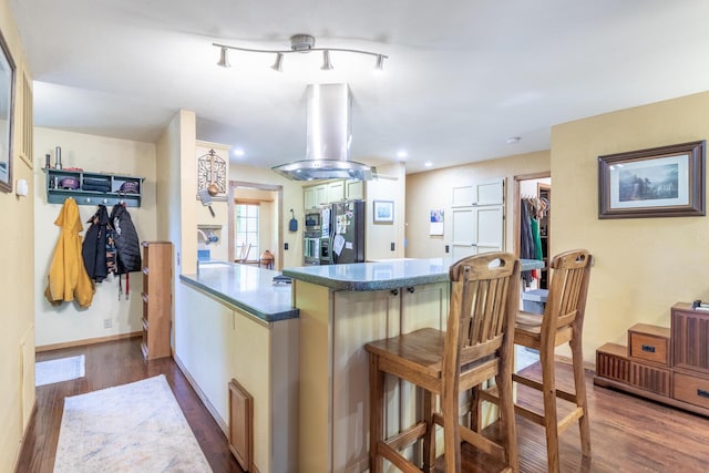 kitchen featuring a breakfast bar, island range hood, a peninsula, black fridge, and dark wood-type flooring