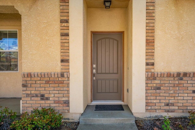 doorway to property featuring stucco siding and brick siding