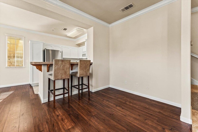 kitchen featuring visible vents, freestanding refrigerator, dark wood-style flooring, a breakfast bar area, and white cabinetry