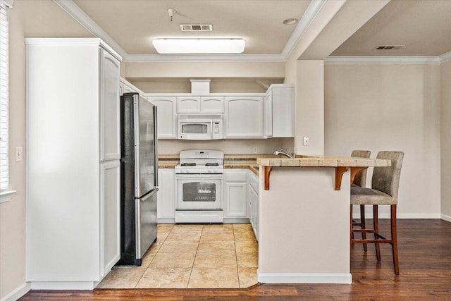 kitchen featuring crown molding, a breakfast bar, white appliances, a peninsula, and visible vents