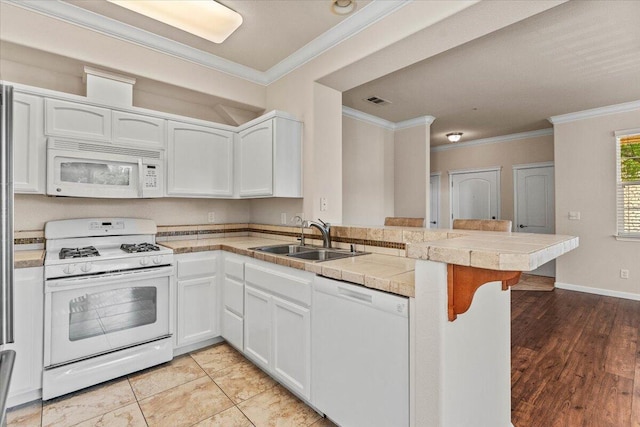 kitchen featuring ornamental molding, a peninsula, white appliances, a kitchen bar, and a sink