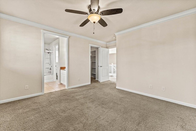 unfurnished bedroom featuring crown molding, baseboards, a spacious closet, carpet, and ensuite bath