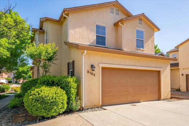 traditional-style home featuring a garage, driveway, and stucco siding