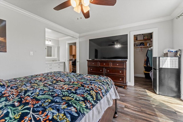 bedroom featuring ornamental molding, freestanding refrigerator, wood finished floors, a walk in closet, and a ceiling fan