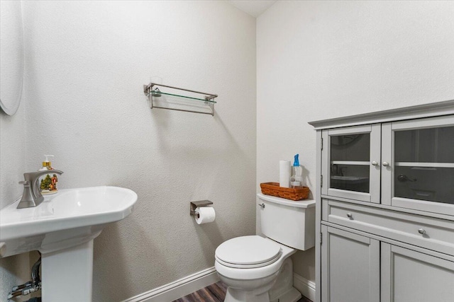 half bathroom with toilet, baseboards, a sink, and wood finished floors