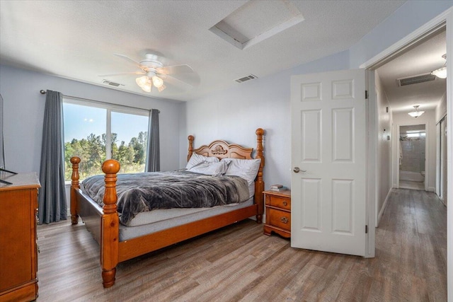 bedroom with a ceiling fan, attic access, wood finished floors, and visible vents
