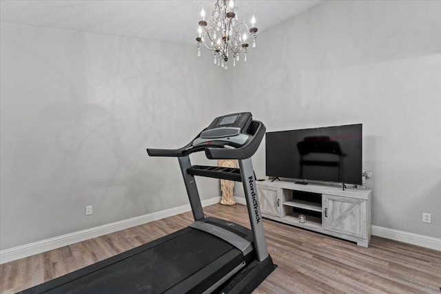exercise area with baseboards, wood finished floors, and a chandelier