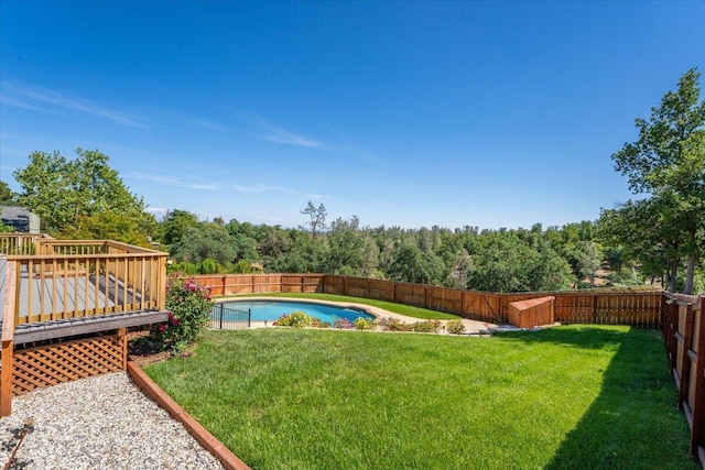 view of yard featuring a fenced backyard, a fenced in pool, a wooden deck, and a wooded view