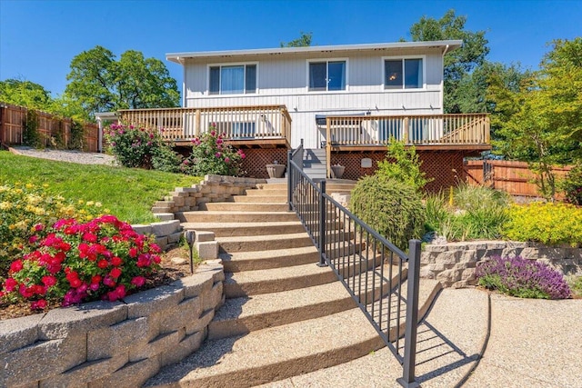 back of property with fence, a wooden deck, and stairs
