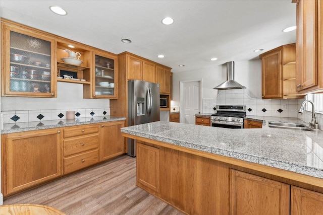 kitchen featuring a peninsula, wall chimney exhaust hood, a sink, backsplash, and stainless steel appliances