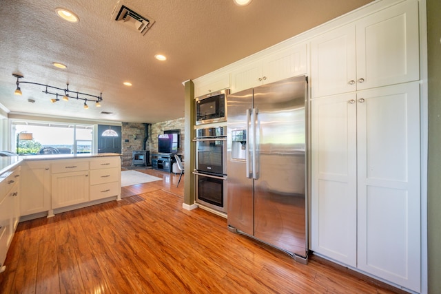 kitchen with appliances with stainless steel finishes, a wood stove, a textured ceiling, open floor plan, and visible vents