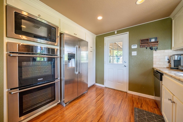 kitchen featuring light wood finished floors, stainless steel appliances, baseboards, recessed lighting, and white cabinetry