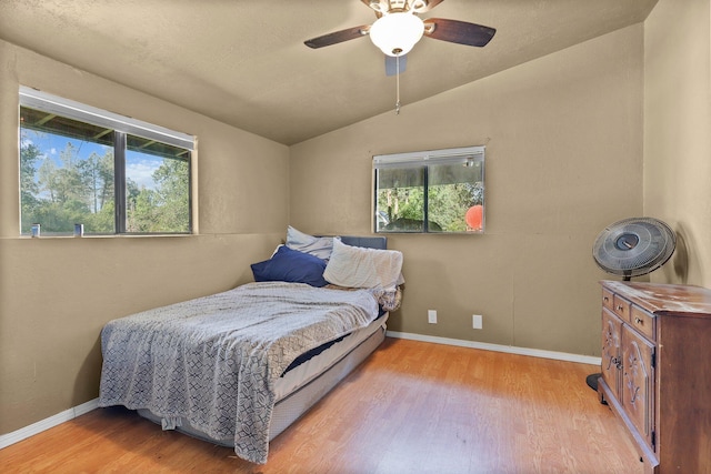 bedroom with baseboards, multiple windows, light wood-style flooring, and lofted ceiling